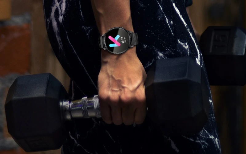 Mulher com smartwatch Kumi GW5 no pulso e alteres na mão.